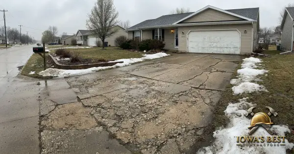 Cracked concrete driveway with freeze-thaw damage in front of Iowa home with melting snow